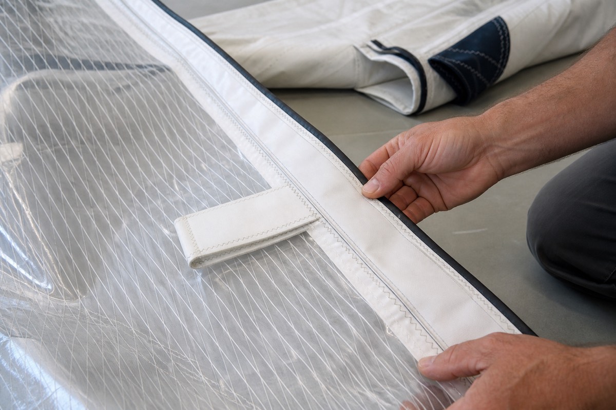 Hands checking stitching and a batten pocket along a sail leech