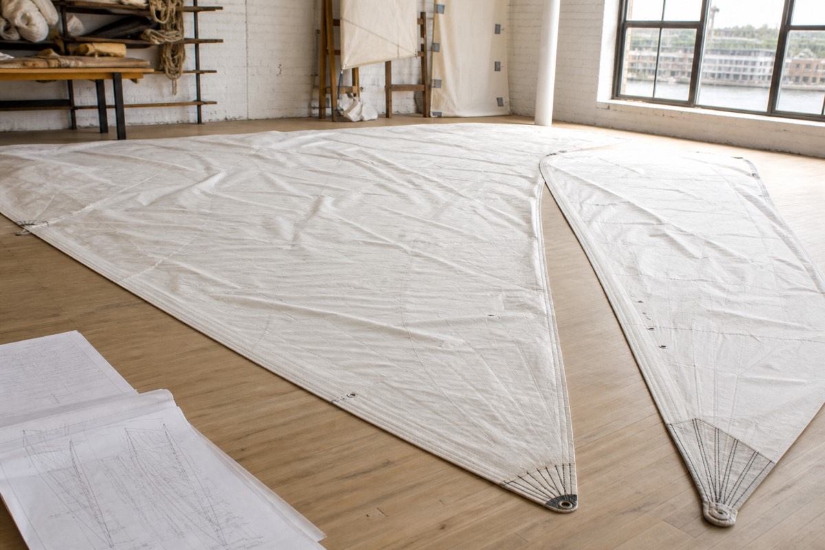 A mainsail and headsail spread across a loft floor beside a sail plan